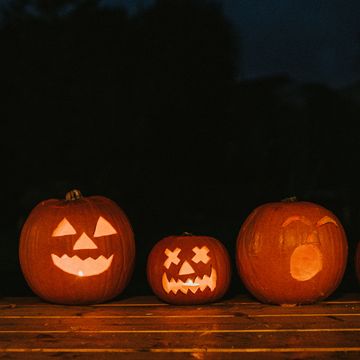 a row of various sized carved hallowe'en pumpkins with different facial expressions glowing in the dark space for copy